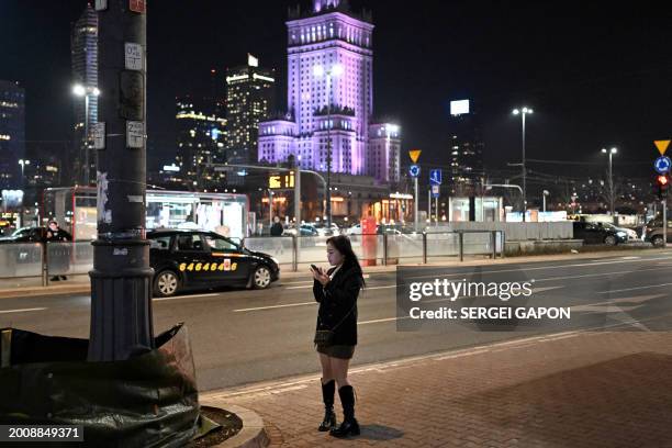 Woman uses her mobile phone as she walks down the street in front of the Palace of Culture and Science, in Warsaw, on February 16, 2024.