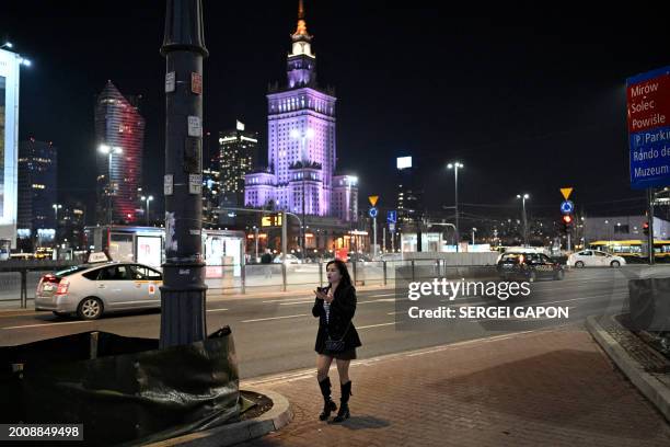 Woman uses her mobile phone as she walks down the street in front of the Palace of Culture and Science, in Warsaw, on February 16, 2024.
