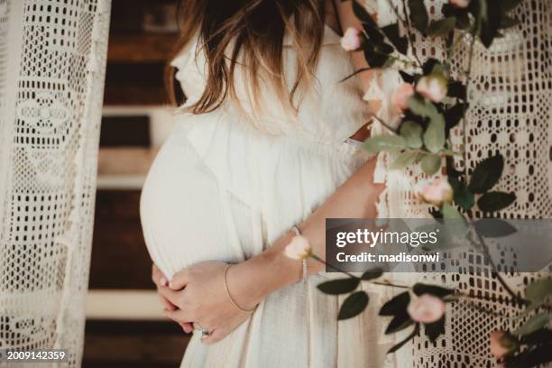 schwangere frau hält ihren bauch in boho-umgebung - pregnant woman in flowers stock-fotos und bilder