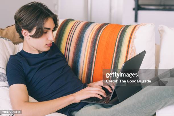 teenage boy using digital tablet while reclining on sofa at home - websurfen stock-fotos und bilder