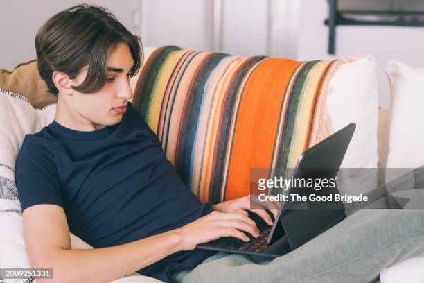teenage boy using digital tablet while reclining on sofa at home - malibu home stock pictures, royalty-free photos & images