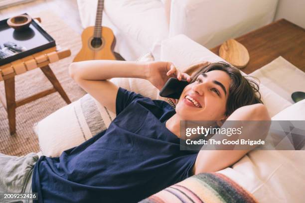 high angle view of happy teenage boy talking on mobile phone while lying at home - malibu home stock pictures, royalty-free photos & images