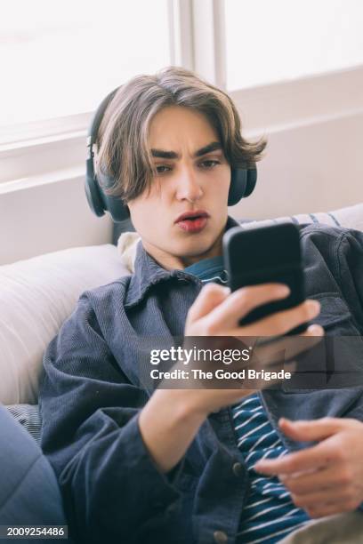 teenage boy with smart phone listening to music on sofa at home - malibu home stock pictures, royalty-free photos & images