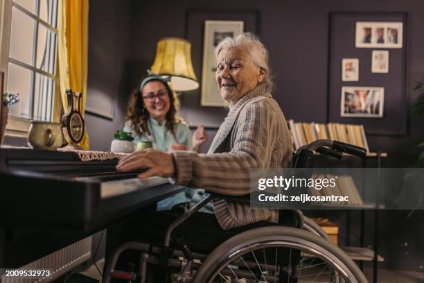 at home, the nurse listens to the senior woman playing the piano - pianist stockfoto's en -beelden