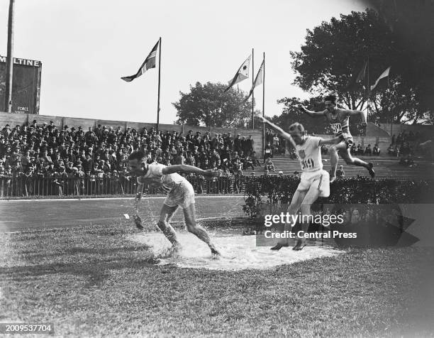 Finnish athlete Ville Ritola leads from American athlete Marvin Rick, as French athlete Paul Bontemps clears a jump during the men's 3000 metres...