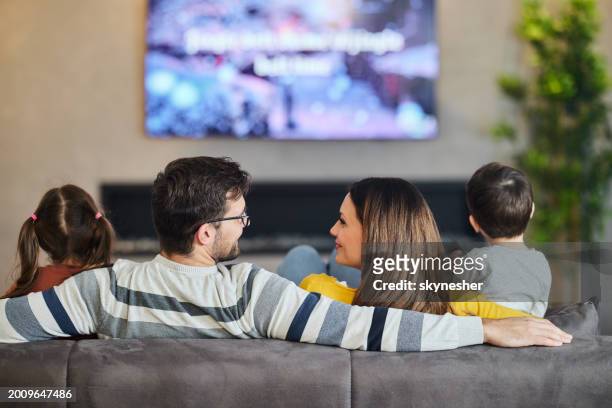back view of a family watching tv at home. - family watching tv from behind stockfoto's en -beelden