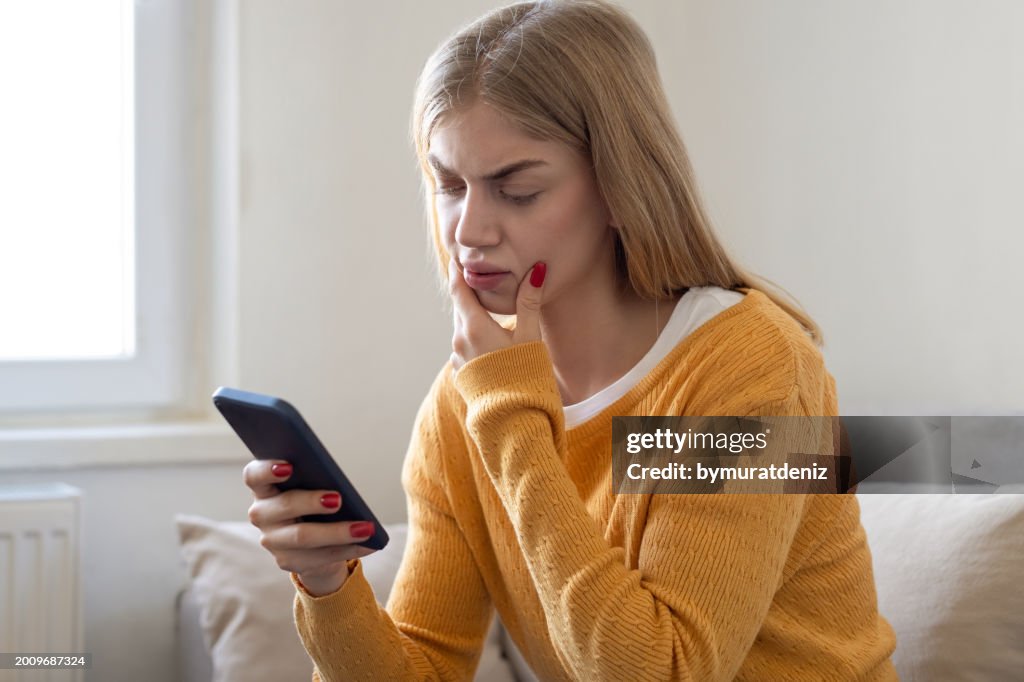 Mulher preocupada sentada no sofá em casa e segurando o telefone