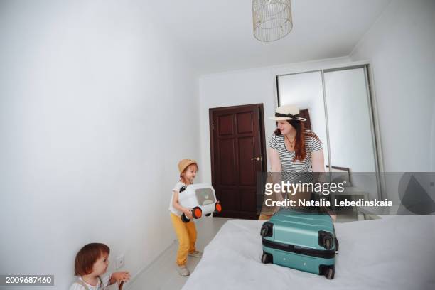 mom and two sibling children with suitcases arrived in a hotel room, putting suitcases on the bed - hotel confirmation stock pictures, royalty-free photos & images