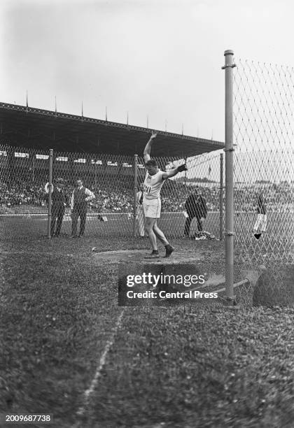 American athlete Fred Tootell competes in the men's hammer throw event, with officials observing from the other side of the chainlink 'hammer cage',...