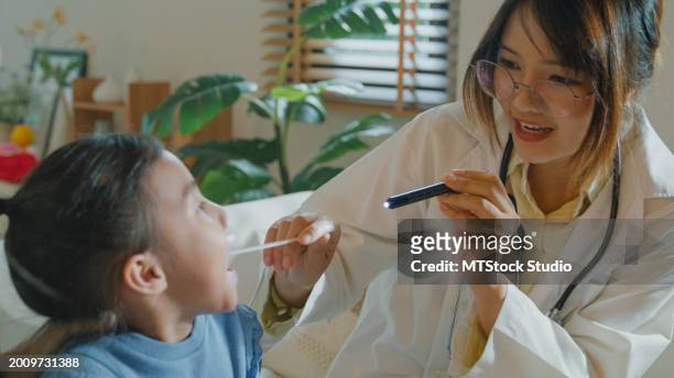 closeup of a female doctor checks the mouth and throat of a girl who gets sick and has a high fever at home. illness girl stays with her mom with a medical condition and family wellness. - girl tongue doctor stockfoto's en -beelden