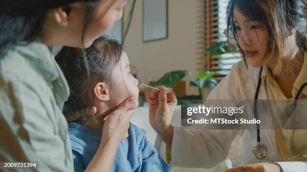 menina asiática, que fica doente e tem febre alta, faz swabs nasais de um médico em casa. doença menina fica com a mãe com uma condição médica e bem-estar familiar. - teste de diagnóstico rápido - fotografias e filmes do acervo