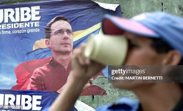 Man sips coffee in front of a campaign poster of Alvaro Uribe, in Soacha Bogota, 25 May 2002. AFP PHOTO/Martín BERNETTI Un hombre bebe café frente a...