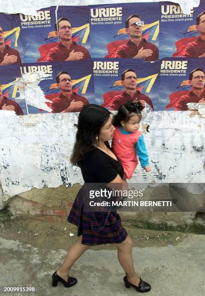 Mother holding her child, walks in front of political propaganda posters of presidential candidate Alvaro Uribe in Soacha near Bogota, 25 May 2002....