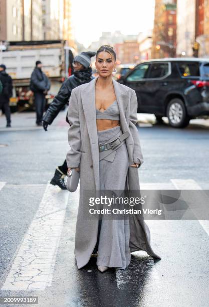 Camila Coelho wears grey oversized coat, cropped top, belt, high waisted skirt, bag outside Michael Kors on February 13, 2024 in New York City.