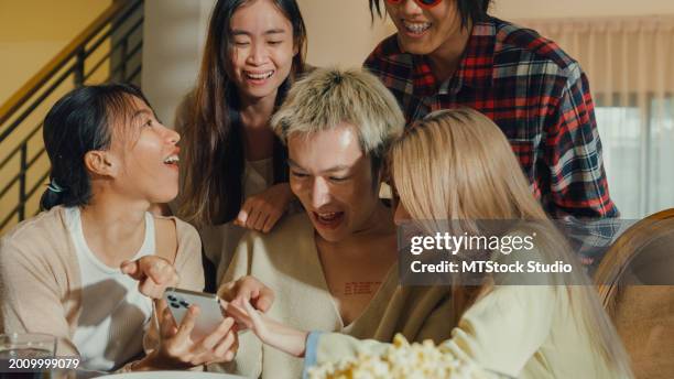 group of young asian people watching smartphone and having fun sitting at dining table at home. multicultural friends enjoying spending together college house party. - virtual thanksgiving stock pictures, royalty-free photos & images