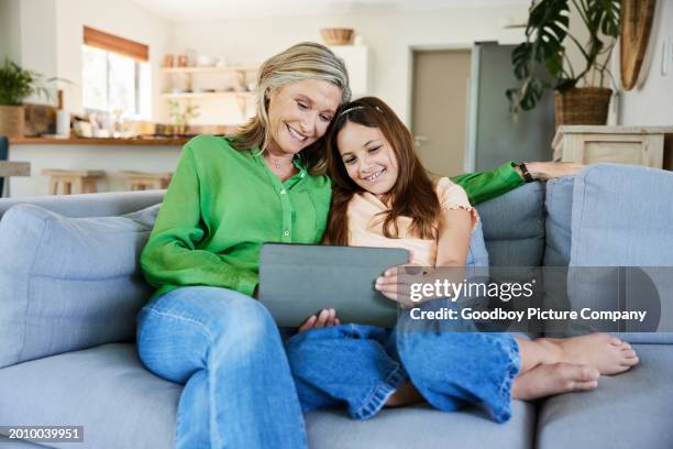 smiling girl and her grandma using a tablet on a living rom sofa - kids rom stock pictures, royalty-free photos & images