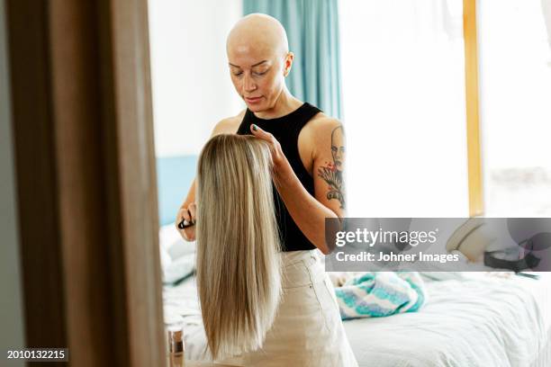 bald woman with cancer holding blond wig standing in bedroom at home - peluca fotografías e imágenes de stock