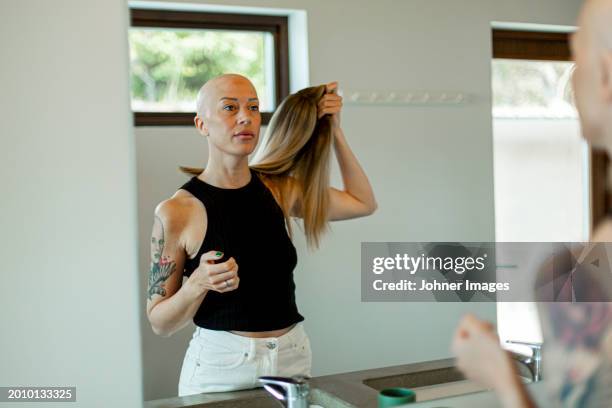 reflection of woman with cancer removing wig while standing in bathroom - peluca fotografías e imágenes de stock