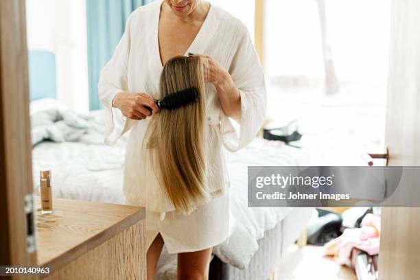 midsection of woman combing blond wig while standing in bedroom - peluca fotografías e imágenes de stock