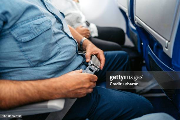 senior man fastening his seatbelt in an airplane - belt stock pictures, royalty-free photos & images