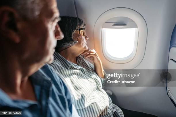 älteres paar, das aus dem fenster eines flugzeugs schaut - fahrzeugschein stock-fotos und bilder