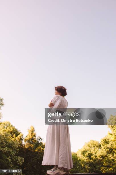 portrait of young woman standing against green trees and blue sky during summer - blue blouse stock pictures, royalty-free photos & images