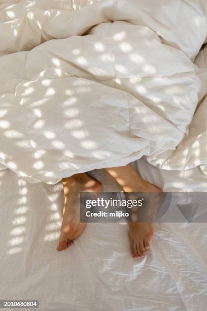 frauenbeine beim schlafen im bett mit decke bedeckt - bettbezug stock-fotos und bilder