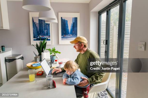 side view of a mature red headed man working from home with his baby daughter on his lap - working dad stock pictures, royalty-free photos & images