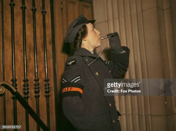 Woman officer of Royal Air Force Police , wearing an 'RAFP' armband with her uniform, blows a whistle which she holds in her gloved left hand, during...