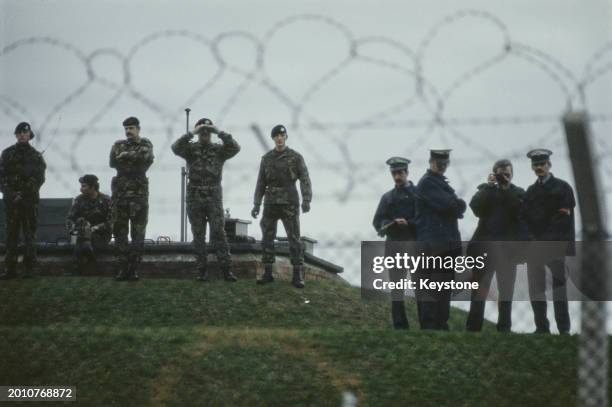 Military personnel and military police seen through a chainlink fence at Greenham Common Women's Peace Camp at RAF Greenham Common, in the parishes...