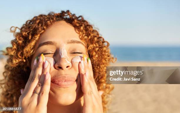 donna felice sorridente che applica la crema solare sul viso sulla spiaggia al tramonto. - trattamento per la pelle foto e immagini stock