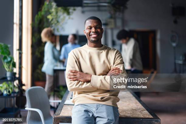 selbstbewusster junger mann lächelt in lässiger büroumgebung - cool modern mann büro business stock-fotos und bilder