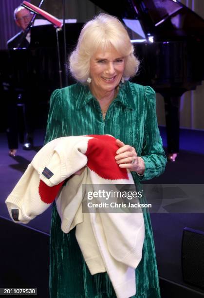 Queen Camilla smiles as she holds gifts of Valentine's Day jumpers with red hearts displayed on them, for herself and King Charles III at the...