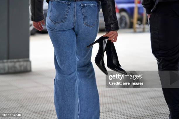 young woman returning from a meeting with friends with her black shoes in her hand because of a broken heel. - woman in broken shoe heel stockfoto's en -beelden