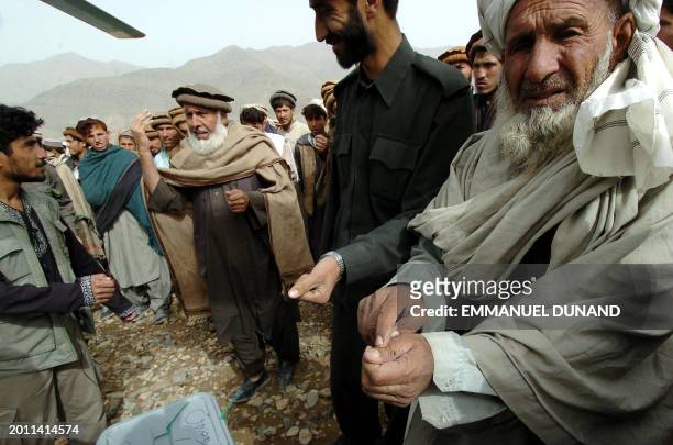 An Afghan villager and a policeman display their finger marked with indelible ink while a village elder says to election field coordinator Mohamad...