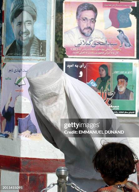 An Afghan woman talks to her child while walking by electoral posters in the northern city of Mazar-i-Sharif, 03 October 2004. Afghanistan is set to...