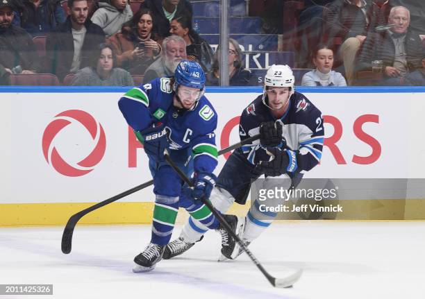 Quinn Hughes of the Vancouver Canucks and Sean Monahan of the Winnipeg Jets battle for the puck during the first period of their NHL game at Rogers...