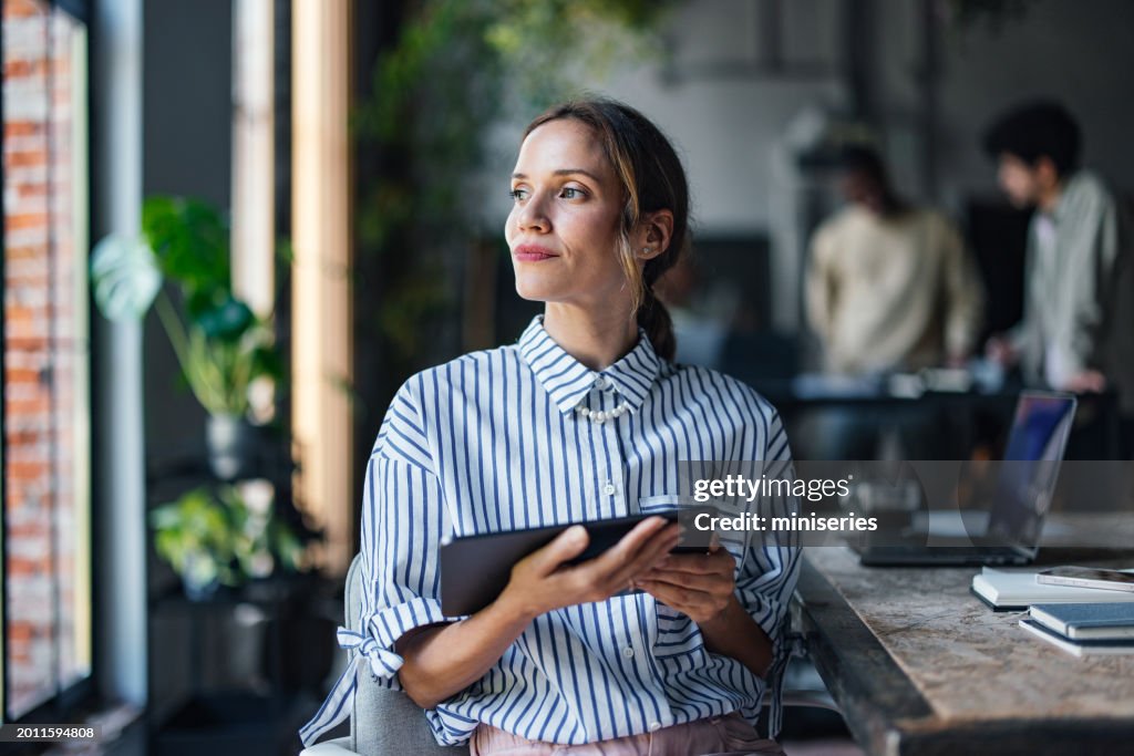 Professional Woman with Tablet Looking Thoughtful in Office