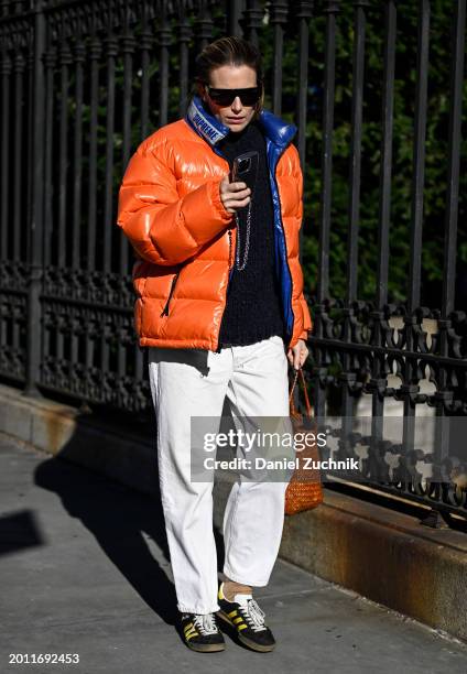 Dree Hemingway is seen wearing a orange and blue puff jacket, blue sweater, white pants, black and yellow sneakers, brown bag and black sunglasses...