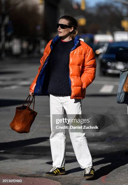 Dree Hemingway is seen wearing a orange and blue puff jacket, blue sweater, white pants, black and yellow sneakers, brown bag and black sunglasses...