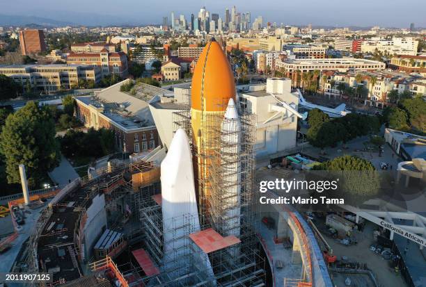 In an aerial view, construction continues around the retired NASA Space Shuttle Endeavour, covered in protective white wrapping, standing mated to...