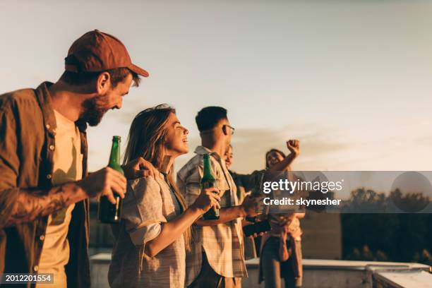 cheerful friends having fun while drinking beer on a roof. - sunset party stock pictures, royalty-free photos & images