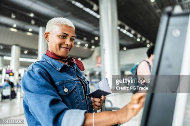 mature woman using self service check-in machine at airport - self service stockfoto's en -beelden