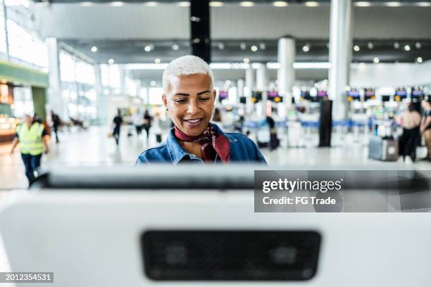 mature woman using self service check-in machine at airport - self service check in stock pictures, royalty-free photos & images