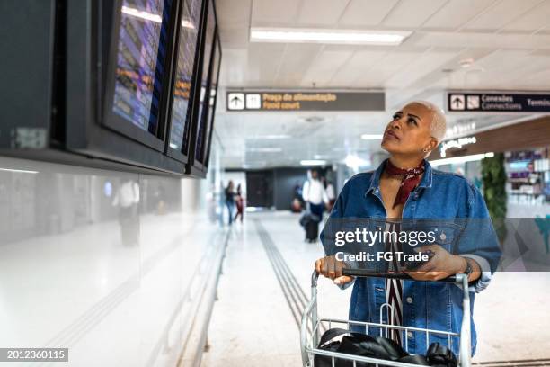 mature woman looking the flight monitor at airport - woman flying scarf stock pictures, royalty-free photos & images