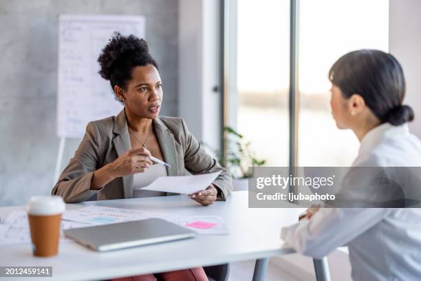 serious business woman, employer holding resume listening young candidate at job interview. - conformiteit stockfoto's en -beelden