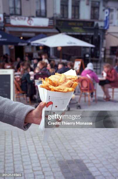 People are eating French Fries on Place Jourdan on February 17, 2024 in Brussels, Belgium. Frying the potatoes in oil, topping them with salt, adding...