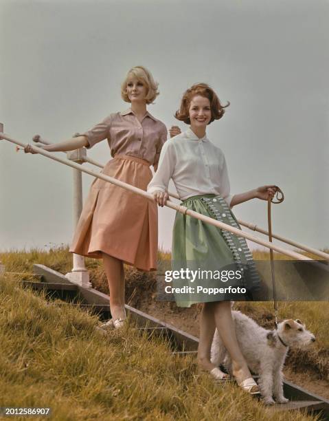 Two female fashion models posed wearing, on left, a blouse and peach coloured summer skirt and, on right, a white blouse and light green knee length...