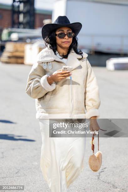 Guest wears cowboy hat, shearling jacket, creme white skirt, heart shaped teddy bag outside Brandon Maxwell on February 14, 2024 in New York City.