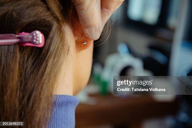 rear view of head of woman having piercing procedure done, master showing ear of customer with new earrings in earlobe. - piercing stock pictures, royalty-free photos & images